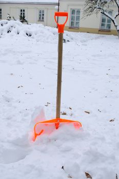 orange plastic snow clean tool in winter snowdrift snow heap and house in background.