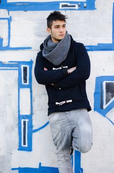 Attractive guy standing against graffiti covered wall, modern clothes
