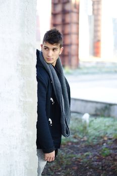 Handsome young man standing behind white wall and looking over it