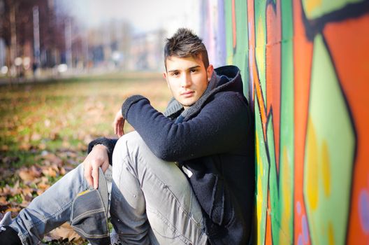 Handsome young man sitting on ground against colorful graffiti covered wall