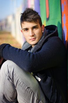 Attractive young man sitting on ground against colorful graffiti covered wall