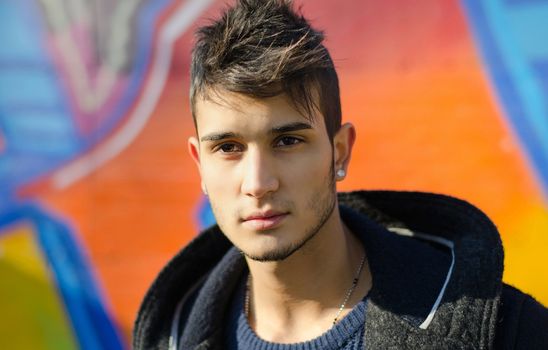 Handsome young man against colorful graffiti covered wall