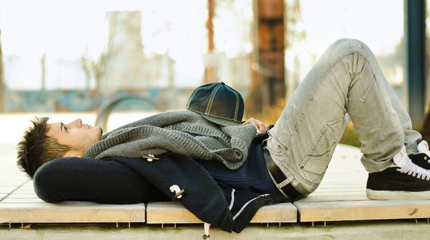 Handsome young man lying on a bench relaxing and looking up