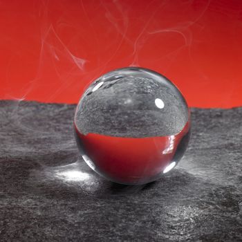 a clear crystal ball on rough dark grey stone surface in front of red back, little smoke around