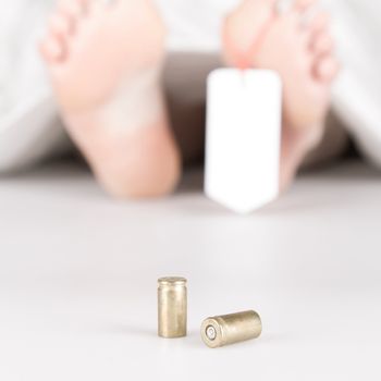 Dead body with toe tag, bullets and a white sheet