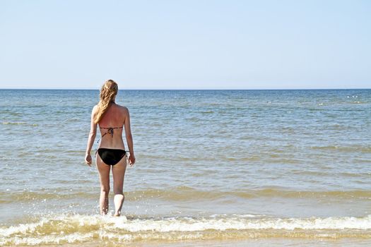 Young blonde woman walking into the ocean