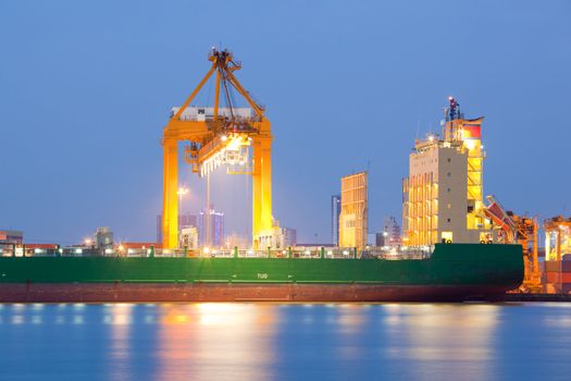 Industrial Container Cargo freight ship with working crane bridge in shipyard at dusk for Logistic Import Export background