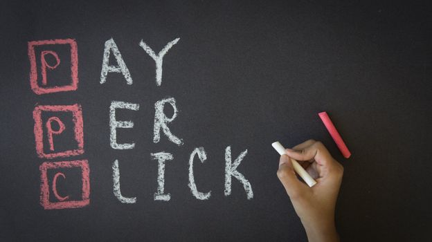 Person writing Pay Per Click with chalk on a Blackboard