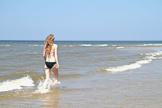 Young woman running through the water from the ocean