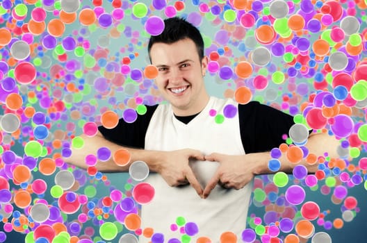 Young man making heart sign with palms with colored balls in the background