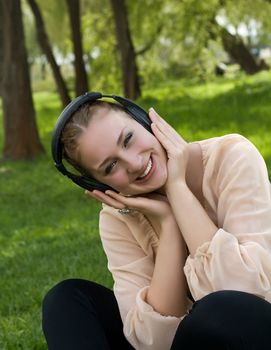 Happy woman sitting on grass listening to music outdoors and laughing
