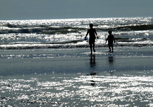 Two Kids Playing on the Beach as the Sun is Glistening on the Water