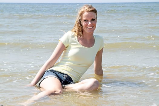 Beautiful happy woman sitting in the water from the ocean