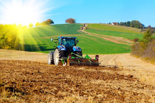 Tractor plows a field in the spring, with sunlight