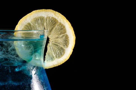 close-up of blue curacao cocktail with slice of lemon on a black background