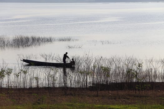 silhouette of fisherman on wood boat at lake.