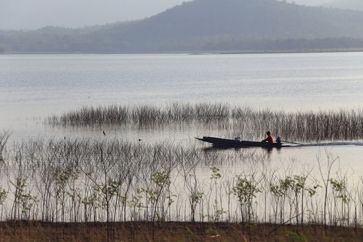 silhouette of fisherman on wood boat at lake.