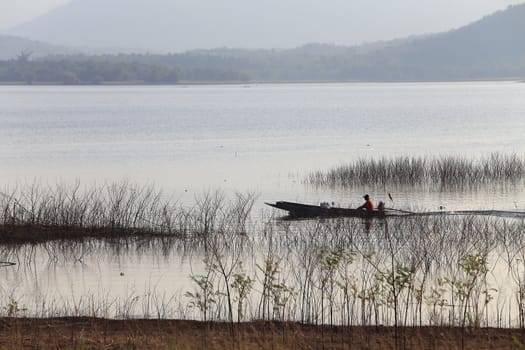 silhouette of fisherman on wood boat at lake.