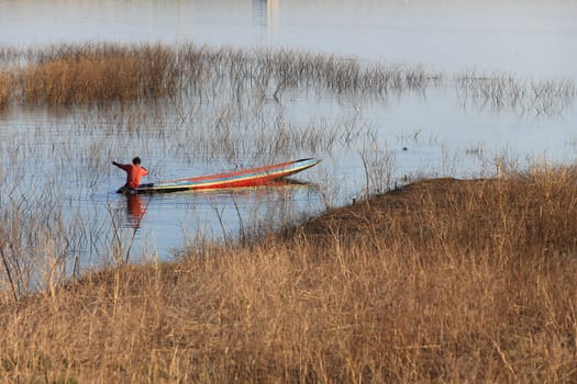 silhouette of fisherman on wood boat at lake.