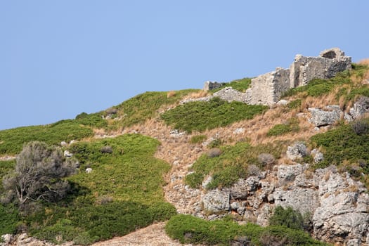 old ruins on the top of a small rock hill filled with grass