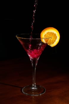 pooring red wine on a cocktail glass with slice of orange