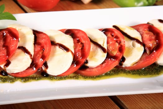 plate of a fresh tomato and mozarela cheese with pesto and balsamic