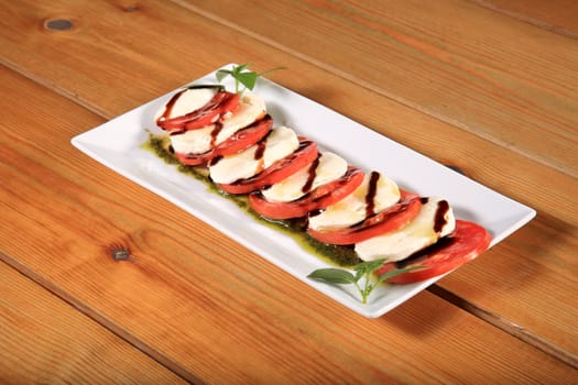 plate of a fresh tomato and mozarela cheese with pesto and balsamic