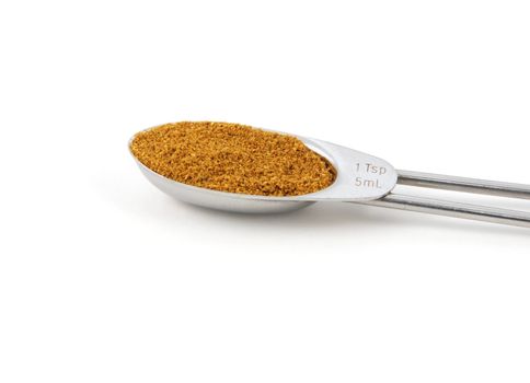 Curry powder measured in a metal teaspoon, isolated on a white background