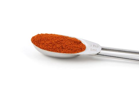 Paprika powder measured in a metal teaspoon, isolated on a white background