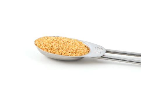 Garlic granules measured in a metal teaspoon, isolated on a white background