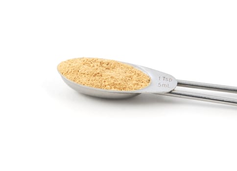 Ground ginger measured in a metal teaspoon, isolated on a white background