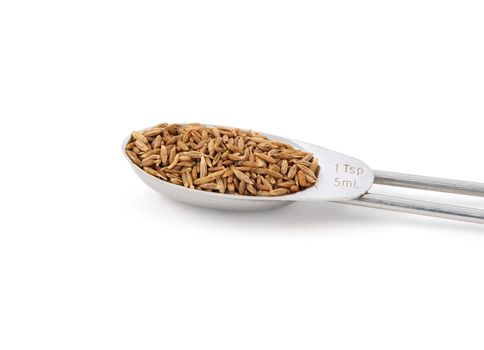 Whole cumin seeds measured in a metal teaspoon, isolated on a white background