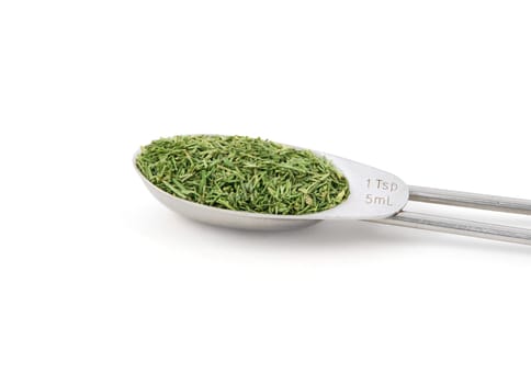 Dill tops measured in a metal teaspoon, isolated on a white background