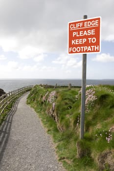 warning sign among wild flowers along a cliff walk path in county Kerry Ireland