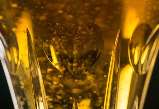 Detail of a cut glass champagne goblet with a heart on the side and filled with drink