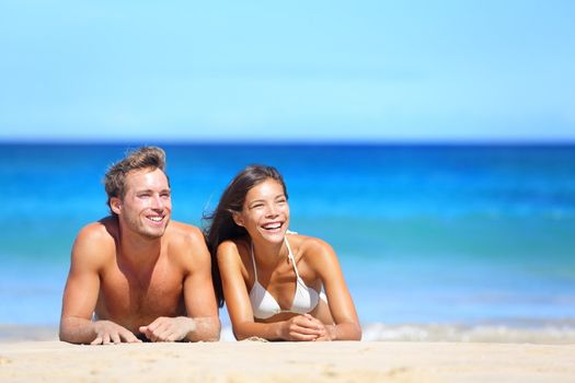 Beach couple looking. Happy multiethnic young couple lying on sand under sunny summer sun. Travel holidays concept. Caucasian man, Asian woman on hawaii.
