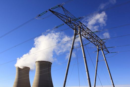 Chimneys of a nuclear power plant with a pylon for renewable energy on blue sky background