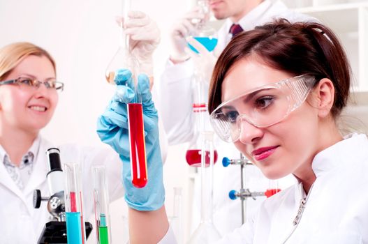 portrait of a beautiful woman chemist, looks at a test tube with red fluid