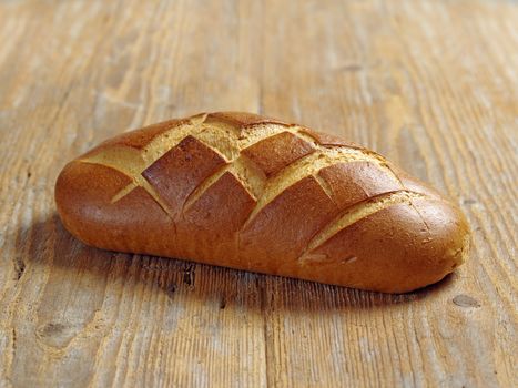 Photo of a single loaf of uncut bread resting on an old wood table.
