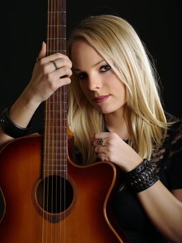 Photo of a young blond female holding an acoustic guitar.