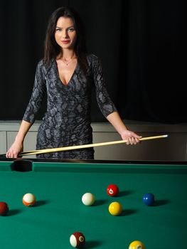Photo of a beautiful brunette holding a pool cue and playing pool.
