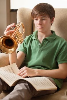 Photo of a teenage male reading sheet music and practicing his trumpet at home.
