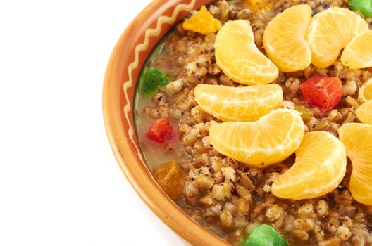 Sweet wheat porridge with dried fruit, lobules tangerine and honey in a clay bowl