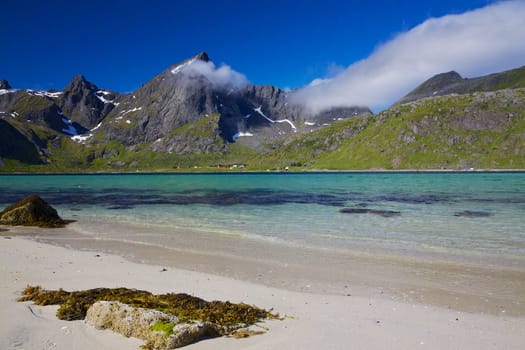 Picturesque mountain peaks towering above fjord with sandy beach on Lofoten islands in Norway