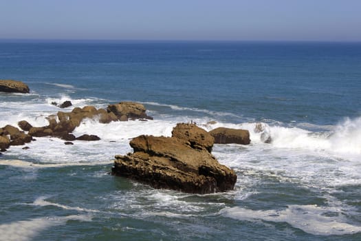 panoramic views of the ocean with its rocks and waves over a blue sky