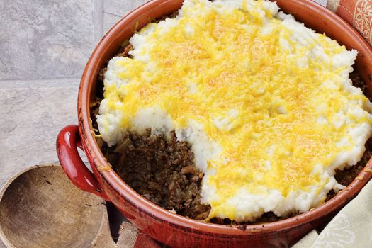 Shepard's Pie in a rustic casserole dish with part taken out exposing inside filling. 
