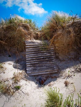 Collapsed sand dune with timber walkway boardwalk hanging over the hill caused by sand and weather erosion.