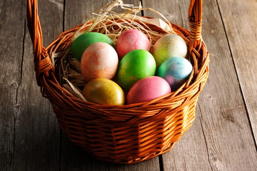 Colored easter eggs in basket on wooden table