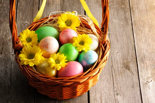 Colored easter eggs in basket on wooden table