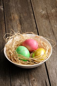 Colored easter eggs in nest on wooden table